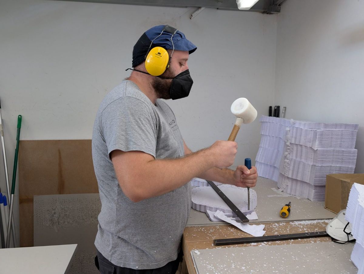 Persones treballant en el taller ocupacional d'AJEM, muntatge de material amb gorres de feina